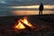 Man standing by the bonfire near the river at sunset