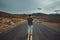 Man standing on empty desert asphalt road waiting and thinking. View from the back