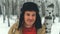 Man standing in forest in winter day. Serious young male wearing beige jacket over red hoodie and earflap hat standing