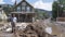 a man standing in front of his flood-damaged house, surrounded by mud and water indicative of a rising river, striving