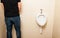 Man standing in front of a white pissoir in bathroom