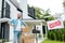 Man standing with hand on hip and holding box near house and board with sold letters