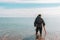 A man standing knee-deep in the water looking for precious metals with a metal detector. Sea and sky on the background