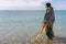 A man standing knee-deep in the water looking for precious metals with a metal detector. Sea and sky on the background. History