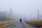 A man standing in the middle of the road next to a old ruined building on a moody misty morning