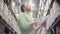 A man is standing near shelves with goods, checking his list, looking for necessary stuff in a warehouse