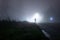 A man standing next to a church, underneath a street light, on a spooky, scary, rural, country road. On a foggy winters night