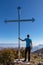 Man standing next to the summit cross of mountain Goli Vrh. Panoramic aerial view on dramatic karst mountain chains Dinaric Alps