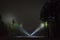 Man standing outdoor at night in forest shining with two flashlights up in dark sky and at trees