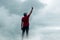 Man standing on rocky outcrop surrounded by white, billowing clouds with his hands reaching the sky