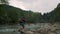 Man standing on rocky shore of river. Hiker touching water in river with hand