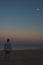 man standing at sea beach looking at moon