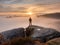 Man stands alone on the peak of rock. Hiker watching to autumn Sun at horizon