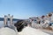 Man stands amid the architecture of Santorini and looks at his watch