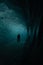 Man stands in an awe-inspiring and mysterious dark ice cave illuminated by a faint light