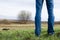 Man stands on burnt field with some remains of green grass and lonely tree on it.