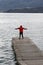 Man stands on a footbridge, jetty, dressed in sweatpants, jogging trousers and hoodie, Lake Como with outstretched arms and lo