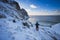 A man stands on a mountain pass with a beautiful view of Kvalvika beach