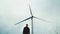 A man stands next to a windmill, a wind turbine, a power line. Renewable energy