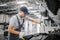 Man stands at opened body of car and works. He is serious and concentrated. He holds black wrench in right hand. Guy