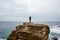 Man stands on a sea cliff, looking into the distance on a dark stormy sea.