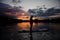 Man stands on sup board on river at sunset.