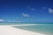 A man stands at the tip of a white sandy beach surrounded by a turquoise lagoon on the island of Fakarava, French Polynesia in the