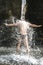 A man stands under a stream of water under a waterfall, summer, hot