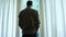 A man stands by the window with curtains in a hotel room, looks at an amazing city landscape