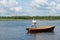 A man stands in a wooden boat in the middle of the lake and fishing for spinning