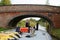 Man steering canal boat under bridge