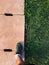 Man step up on right foot in green sneaker. cement drain grate and green grass with abstract background