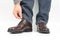 Man straightens his shoelaces on brown classic shoes on a white background