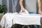 A man strokes linen with an electric iron on an ironing board. Household