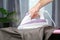 A man strokes linen with an electric iron on an ironing board. Household