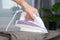 A man strokes linen with an electric iron on an ironing board. Household