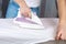 A man strokes linen with an electric iron on an ironing board. Household