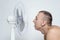 Man with stubble on his face suffers from the heat and trying to cool off near the fan