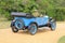 Man in suit is driving the old timer car in Beaulieu in England in the summer.