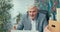 Man in suit with gray hair leads remote conversation from office sitting at desk in front of laptop waving