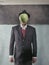 Man in a suit and hat standing near the wall with a green apple in front of his face
