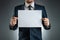 A man in a suit holds a white A4 sheet, mockup, layout. Concept for business lettering, blank. Shot on a gray background