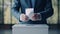 a man in a suit lowers a ballot with his voting vote into a voting basket