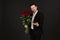 man in suit is posing on black background with ring and red roses in hands.