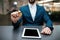 Man in suit with smartwatch hold bitcoin in hand sits at table with tablet in office interior