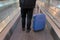 Man with a suitcase on wheels, photographed from behind, at the airport on a moving walkway