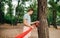 Man in sunglasses and casual clothes hangs a hammock to a tree in the park with a concentrated face, knits slings