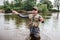 Man in sunglasses stands in water and fishing. He is preparing fly-fishing. Guy holds it in one hand and spoon in the