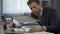 Man surrounded by paperwork at office looking at graphs, head falling on folders