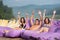 Man is surrounded by two women sitting on a cushioned lounger with his hands raised up and looking to the camera